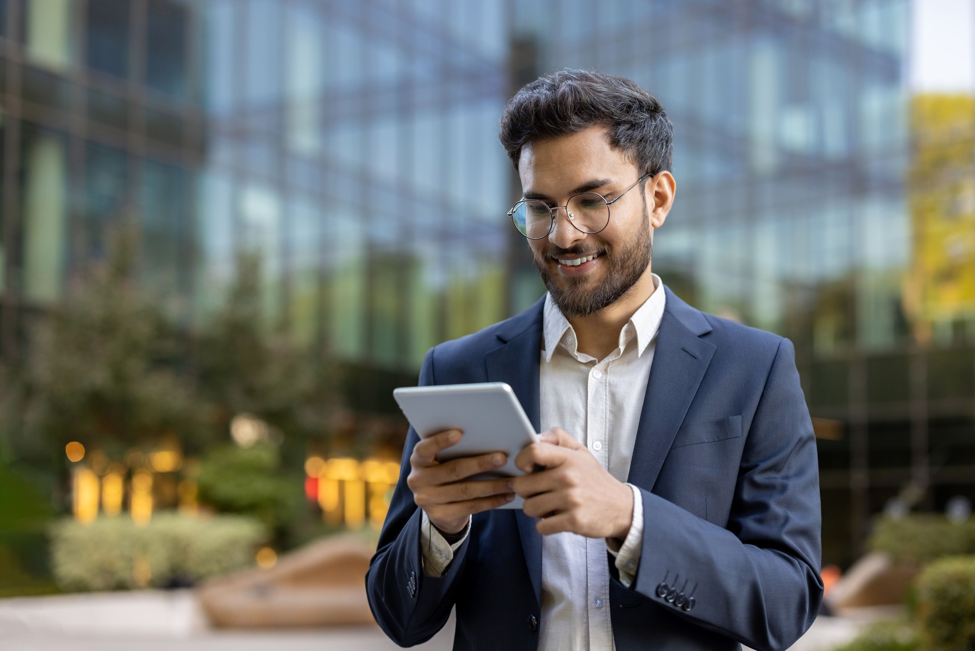 Smiling businessman using a digital tablet outside modern office building
